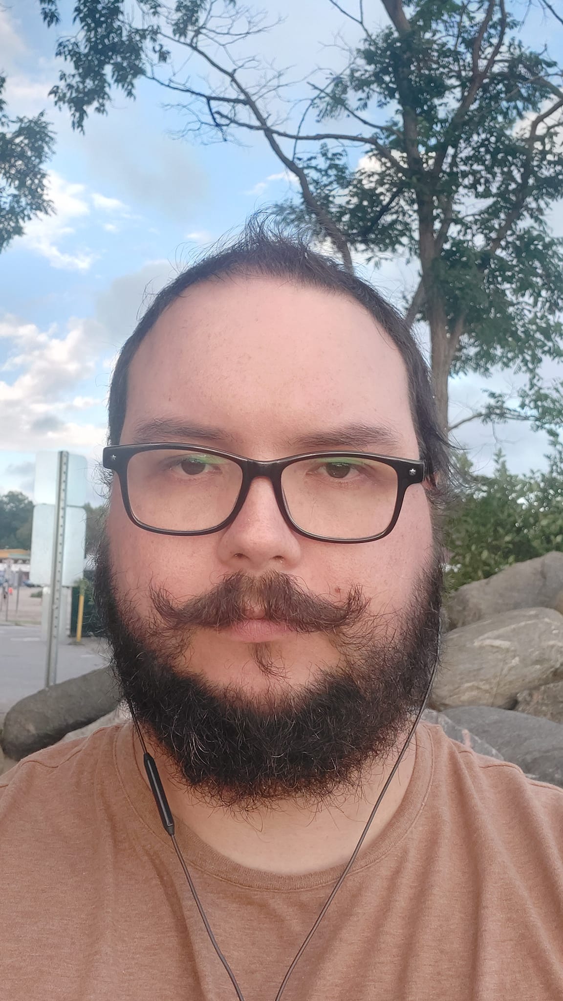 A man short hair and bushy facial hair sits on a rock with more rocks in the background